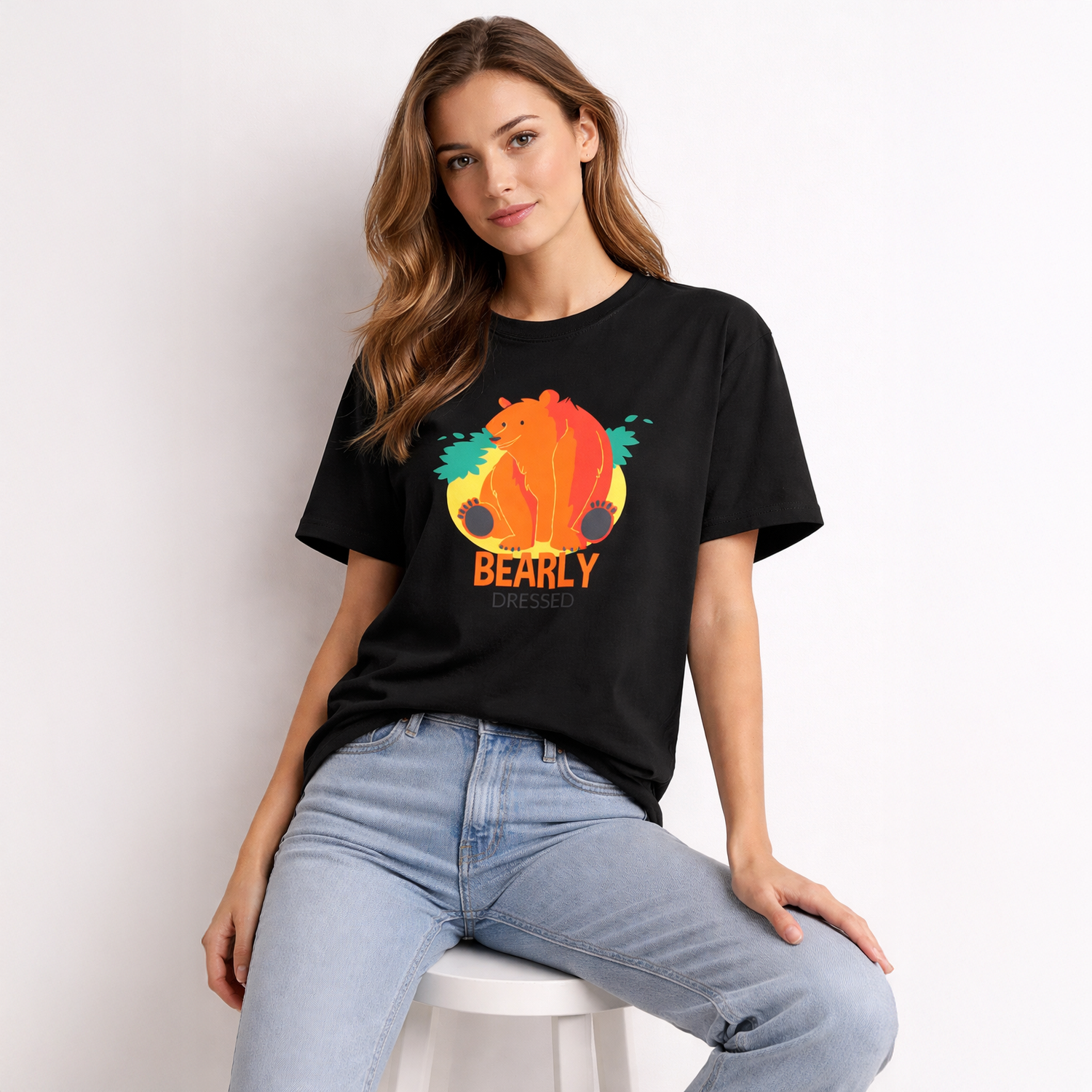 Woman wearing a black t-shirt with a colorful bear graphic and 'BEARLY' text, sitting on a white stool.
