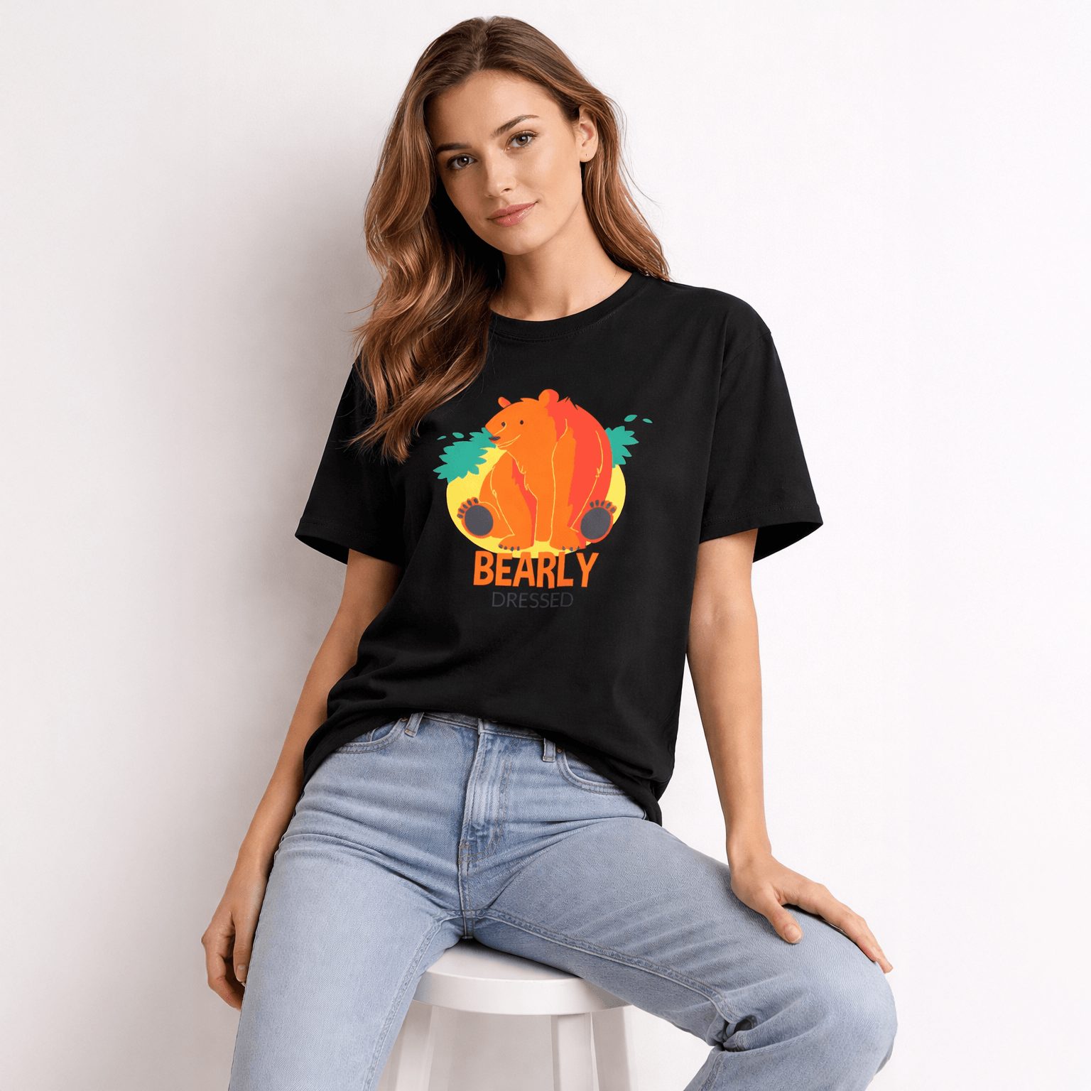 Woman wearing a black t-shirt with a colorful bear graphic and 'BEARLY' text, sitting on a white stool.