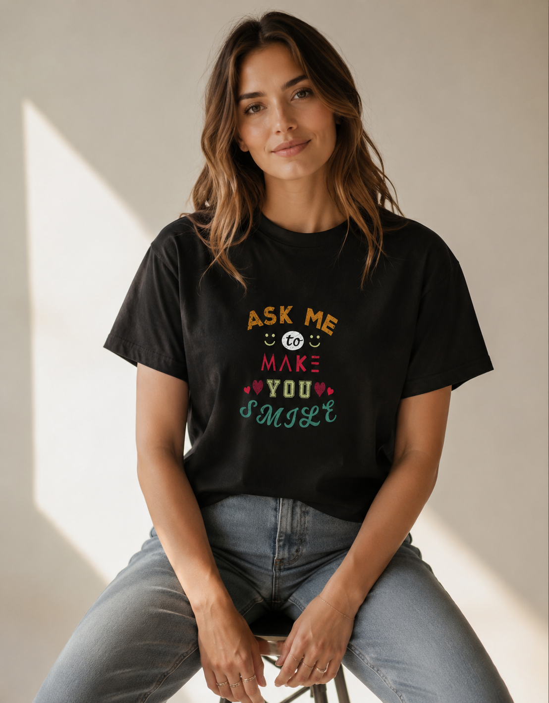 Woman wearing a black t-shirt with colorful text sitting on a stool.