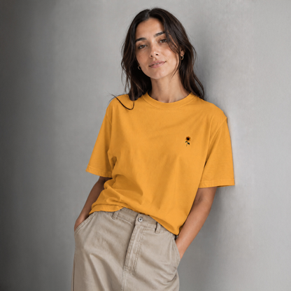 Woman wearing a mustard yellow t-shirt with a small black design against a gray background